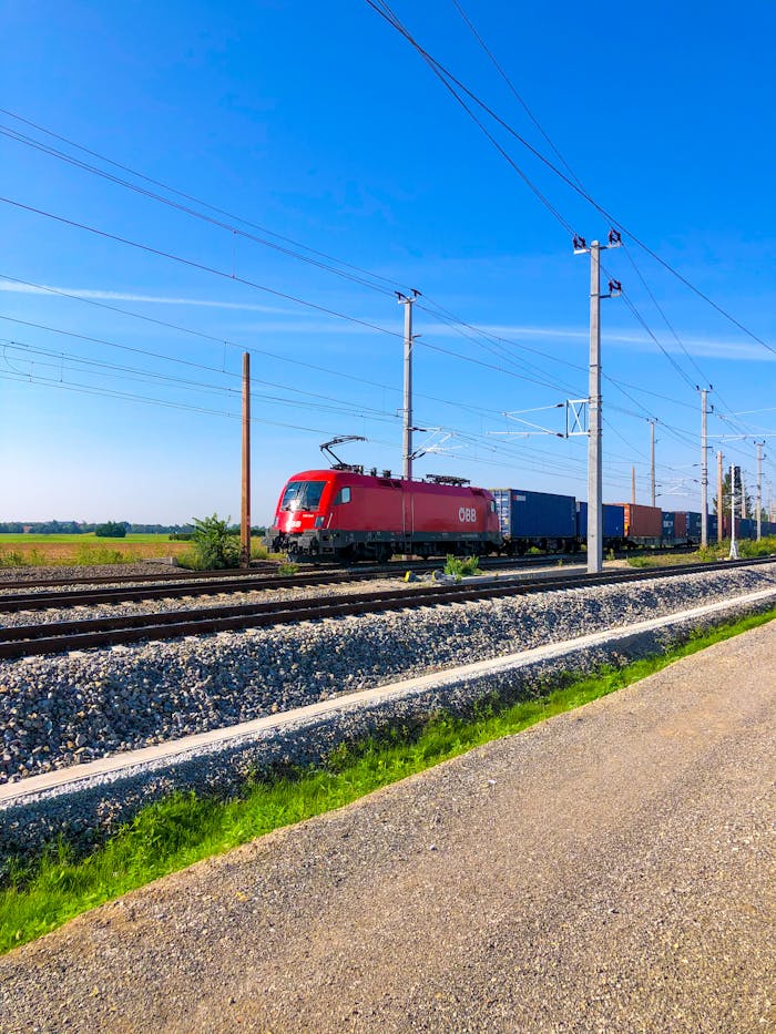Cargo freight train on railway tracks in rural Austria under a clear blue sky.