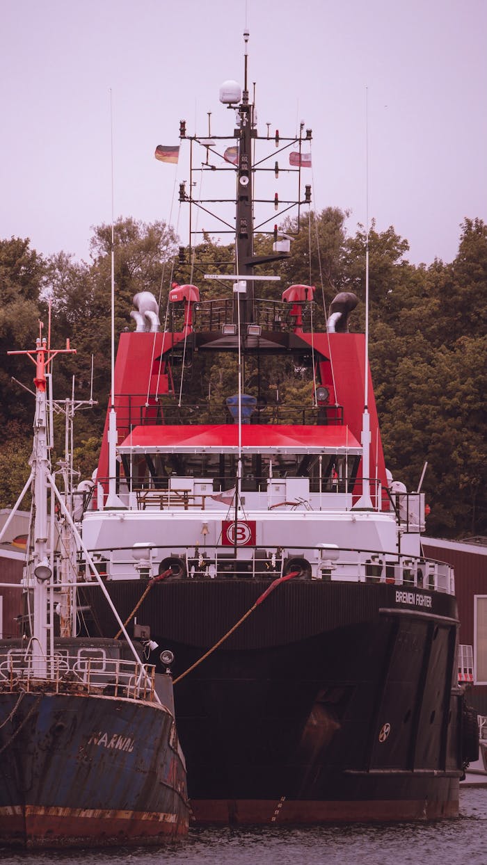 about-us A large cargo ship with a red and black structure docked at a harbor, surrounded by trees.